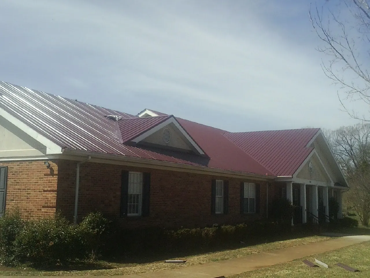 Red metal roof with gabled entries on a long brick building, from a Hail Damage Roof Repair job in Priest River