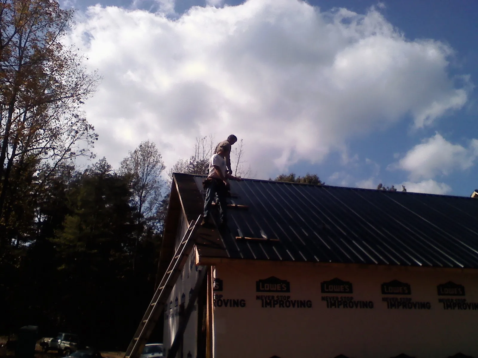 Roofer fastening dark metal panels high against a cloudy sky, from a Roof Inspection job in Priest River