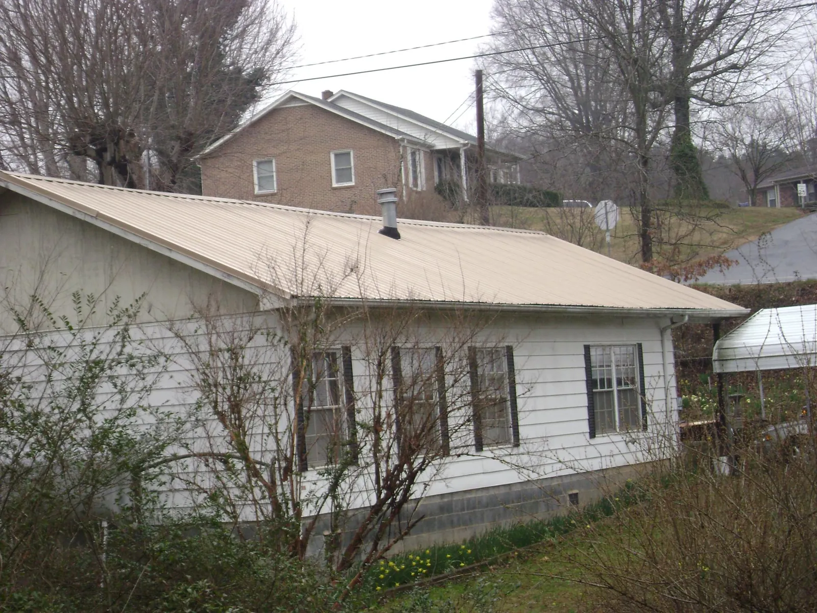Tan metal roof on a white sided house set into a hillside — Commercial Roofing by Roofing Brothers in Priest River